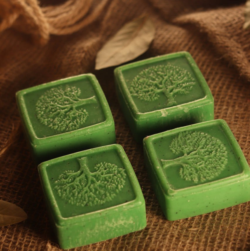 Four green soap bars with tree designs on a brown fabric background